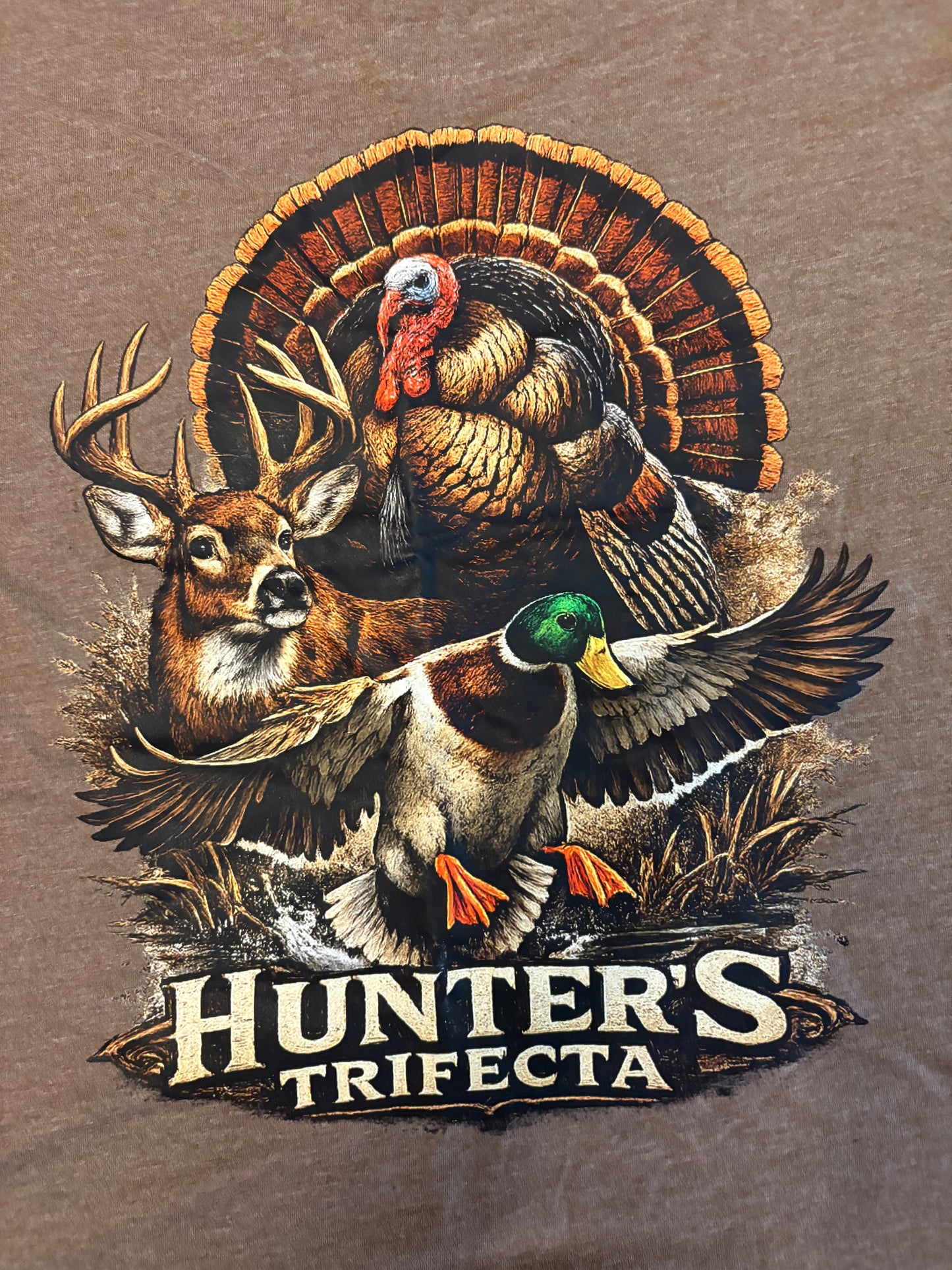 T-shirt design featuring a deer, turkey, and duck with 'Hunter's Trifecta'  back graphic on a brown tee. 